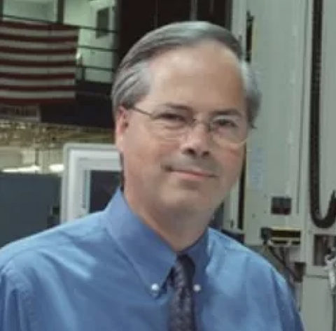 Stephen Murrill headshot, he has gray hair and thin rimmed glasses, and is wearing a blue shirt and tie
